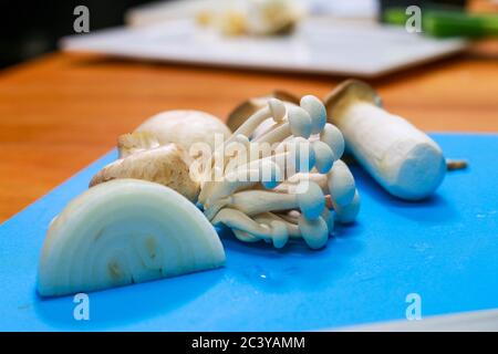 Tranche d'oignon, champignon de hêtre blanc, champignon de trompette sur une planche à découper bleue. Divers types de champignons et ingrédients de cuisson. Banque D'Images