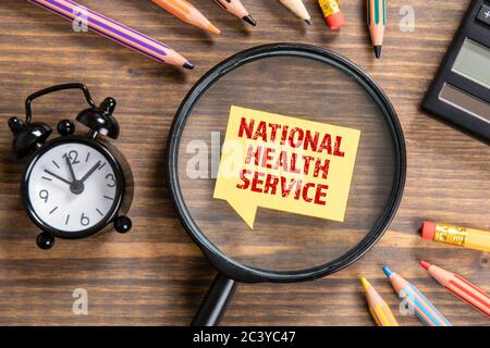 CONCEPT DE SERVICE NATIONAL DE SANTÉ. Loupe noire, bulle de parole et crayons de couleur sur fond en bois Banque D'Images