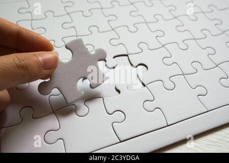 Jeu de pièces de puzzle blanches et main tenant la dernière pièce Banque D'Images