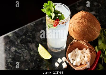 Cocktail au rhum, au sirop de coco, à la coriandre, au citron vert et au piment rouge sur le comptoir en marbre noir Banque D'Images