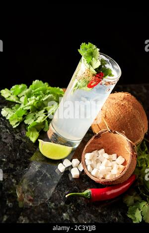 Cocktail au rhum, au sirop de coco, à la coriandre, au citron vert et au piment rouge sur le comptoir en marbre noir Banque D'Images