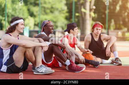 Équipe diversifiée de joueurs de basket-ball professionnels parlant pendant leur pause de jeu à l'arène extérieure, espace vide Banque D'Images