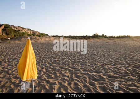 Parasol jaune fermé sur la plage de sable au coucher du soleil Banque D'Images