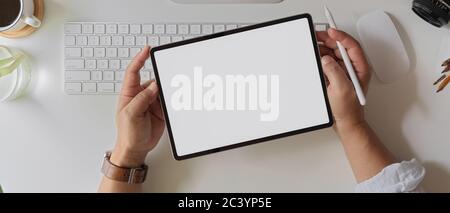 Photo d'un homme d'affaires tenant une tablette à écran vide au-dessus du clavier d'ordinateur et des fournitures sur un bureau blanc Banque D'Images