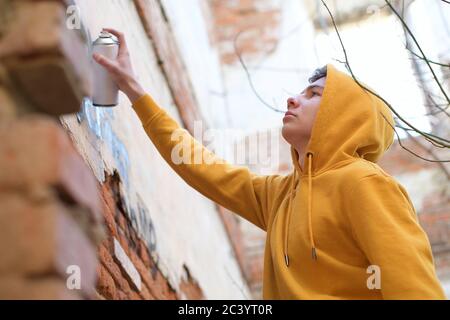 Un adolescent tient une bombe dans sa main et place des inscriptions sur le mur Banque D'Images