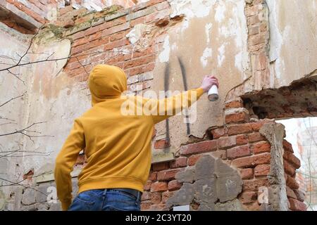 Un jeune homme tire sur le mur d'un bâtiment abandonné. L'adolescent utilise de la peinture en aérosol Banque D'Images