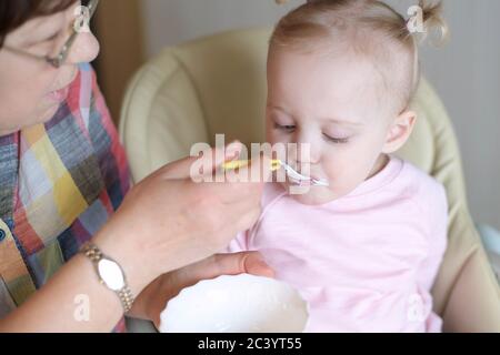 petite fille mangeant du yaourt à la cuillère. Grand-mère nourrit sa petite-fille Banque D'Images