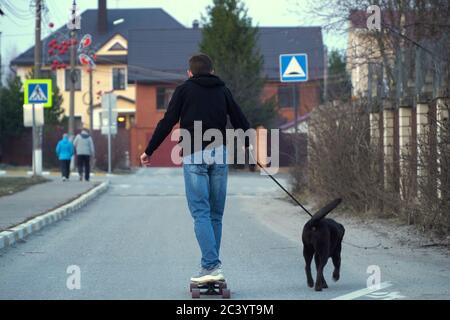 adolescent à bord d'un skateboard et à pied un chien sur un laisse dans un coin couchage Banque D'Images