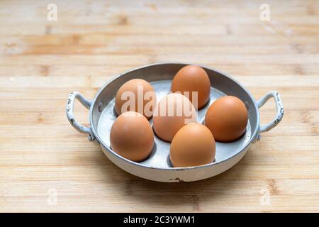 Six poules fraiches fraîches dans une casserole en métal ou un coddler d'oeufs vu de côté sur une table en bois avec copyspace placé au centre Banque D'Images