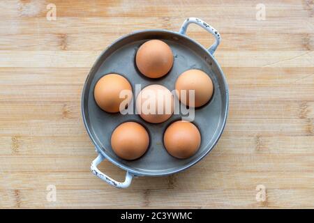 Six poules fraiches dans une casserole en métal ou un coddler à œufs, vue depuis le dessus de la tête sur une table en bois avec un espace d'imitation placé au centre Banque D'Images