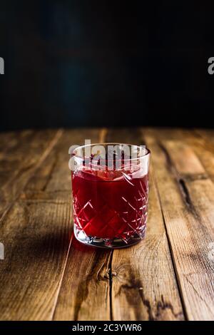 Un cocktail d'hibiscus avec un cube de glace dans un verre de pierre sur une table en bois Banque D'Images