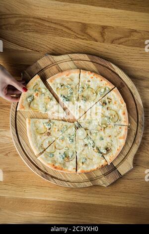 Une femme vole une tranche de pizza d'un plateau rond en bois, photo de dessus Banque D'Images