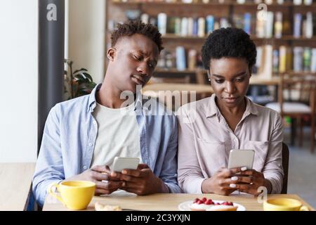 Problème de phishing. Un couple noir est resté dans son smartphone à la date ennuyeuse du café Banque D'Images