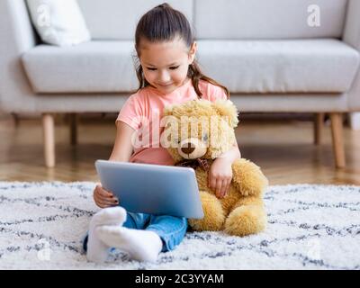 Une fille regarde des carons sur une tablette qui embrasse l'ours en peluche à la maison Banque D'Images