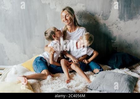 Belle jeune mère blanche câblent ses fils dans le lit. Temps en famille. Portrait de style de vie. Banque D'Images