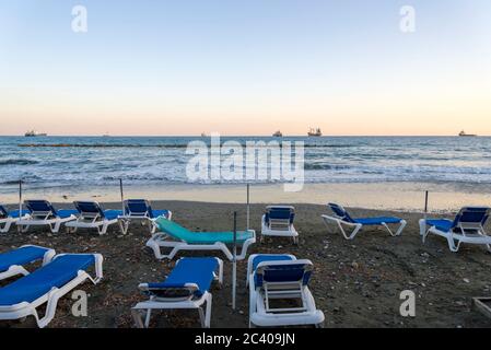 Transats sur la plage de Limassol avec vue sur la mer et les bateaux. Le concept de loisirs et de divertissement. Banque D'Images