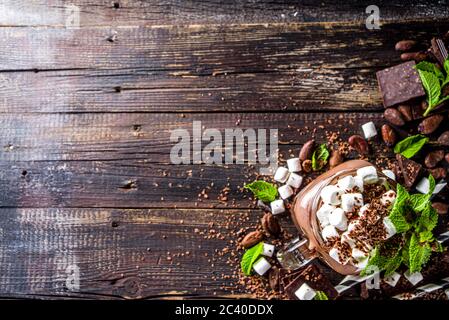 Shake au lait au chocolat avec sauce, guimauves et chocolat râpé, décoré de menthe. Sur une table en bois rustique avec beaucoup de morceaux de chocolat, co Banque D'Images