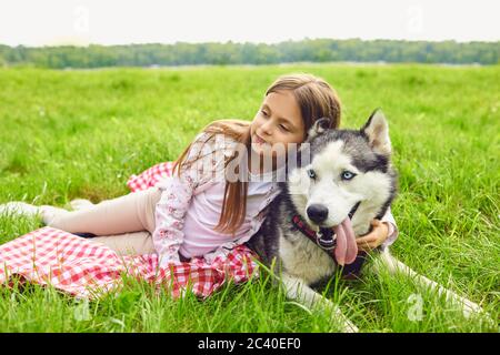 Chien Husky et petite fille reposent sur l'herbe embrassant détendez-vous dans le parc d'été Banque D'Images