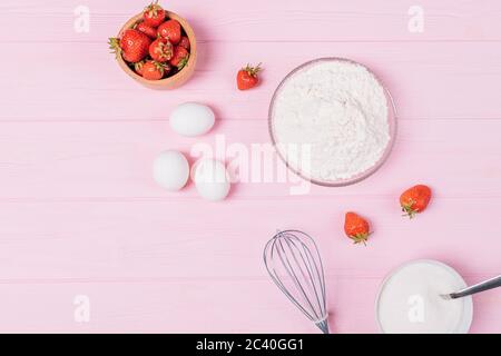 Composition de plat de la pâte à base d'ingrédients pour cuire la tarte aux fraises maison sur fond rose. Banque D'Images