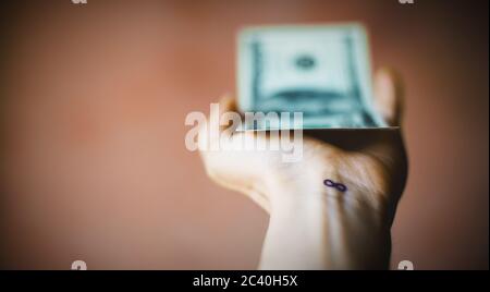 Main floue donnant un dollar facture, sur le poignet un signe d'infini ou le numéro huit. Banque D'Images