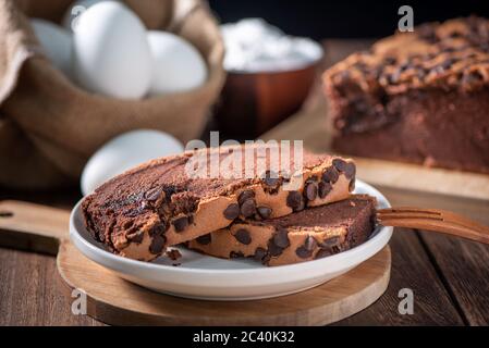 Gâteau éponge traditionnel taïwanais au goût de chocolat (taïwanais castella kasutera) sur une table de fond en plateau de bois avec les ingrédients, gros plan. Banque D'Images