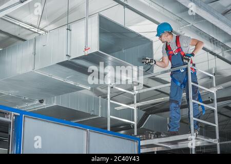 Technicien de CVC de race blanche dans ses 40 ans Test du système de ventilation d'entrepôt nouvellement installé. Système commercial de chauffage, de refroidissement et de ventilation de l'air Banque D'Images