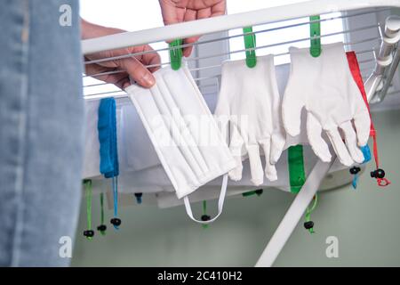 Personne méconnaissable qui pendait des gants réutilisables et qui se masquera après les avoir lavés. Coronavirus et concept de pandémie. Banque D'Images