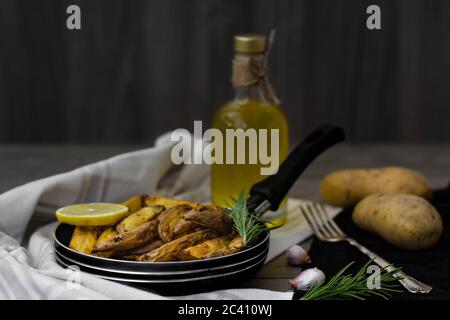 Quartiers de pommes de terre cuits au romarin, à l'ail et au citron dans une petite casserole. Pommes de terre crues, fourchette d'argent vintage, romarin et huile d'olive en arrière-plan. Banque D'Images