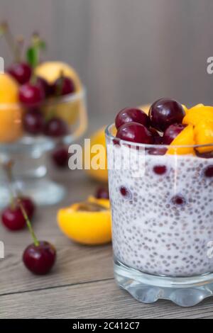 Petit déjeuner végétalien sain avec du pudding aux graines de chia, garni d'abricots et de cerises frais. Plus de fruits et une cuillère d'argent vintage dans le fond en bois. Banque D'Images