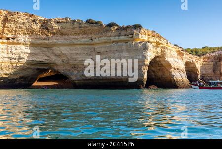 Paysage avec les célèbres grottes de Benagil, ciel bleu clair, falaises de grès et bateau de visite sur la côte de l'Algarve au Portugal Banque D'Images