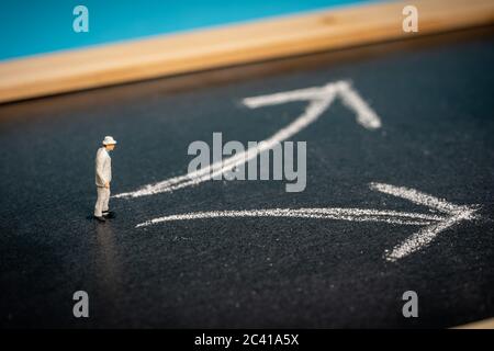 Concept d'entreprise : prise de décision. Homme miniature sur tableau noir avec deux flèches pointant vers des directions différentes Banque D'Images