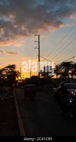 San Miguel de Piura, Piura / Pérou - avril 5 2019: Vue sur un coucher de soleil sur une rue avec des arbres et des voitures en silhouette noire avec le soleil se cachant parmi le t Banque D'Images