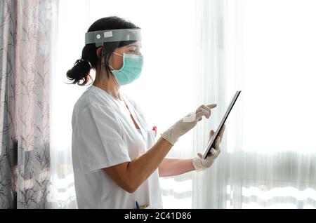 Infirmière avec un écran facial utilisant une tablette. Vue latérale Banque D'Images