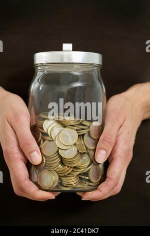 Les mains tiennent un pot avec des pièces de monnaie dans lui Banque D'Images