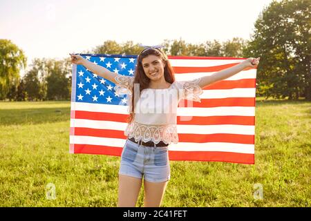 Jeune femme enveloppée dans le drapeau américain dans la campagne. Jour de l'indépendance Banque D'Images