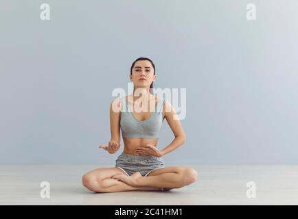 Une enseignante de yoga regardant un appel vidéo avec caméra raconte aux élèves assis dans une position de lotus en classe studio. Banque D'Images