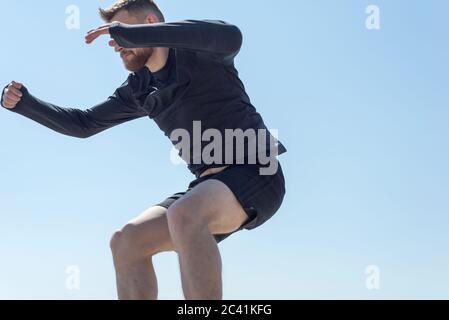 Portrait d'un jeune athlète barbu de vingt-cinq, sautant contre un ciel bleu. Banque D'Images