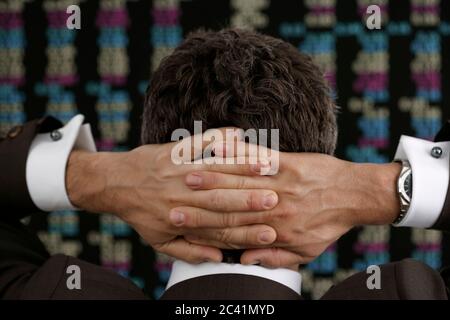 Le courtier en Bourse se tient devant le tableau de bord avec ses mains clapées derrière sa tête Banque D'Images