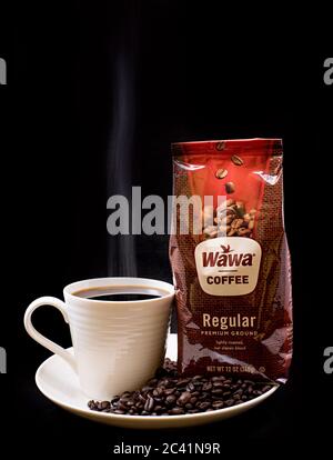 Sac de café Wawa ordinaire en gros plan avec une tasse de café Wawa préparé à la vapeur, une tasse blanche sur une assiette blanche, des grains de café et un fond noir Uni Banque D'Images