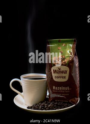 Sac de café Wawa noisette en gros plan avec une tasse de café Wawa à la vapeur, une tasse blanche sur une assiette blanche, des grains de café et un fond noir Uni Banque D'Images
