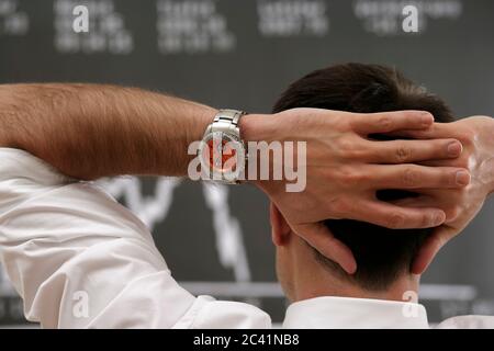 Le courtier en Bourse se tient devant le tableau de bord avec ses mains clapées derrière sa tête Banque D'Images