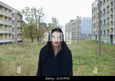 Une jeune femme avec une veste à capuchon se tient entre les maisons abandonnées Banque D'Images