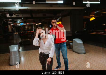 Un homme et une femme caucasiens avec des boules dans leurs mains jouent au bowling et font des grimaces. J'adore le club de bowling Banque D'Images