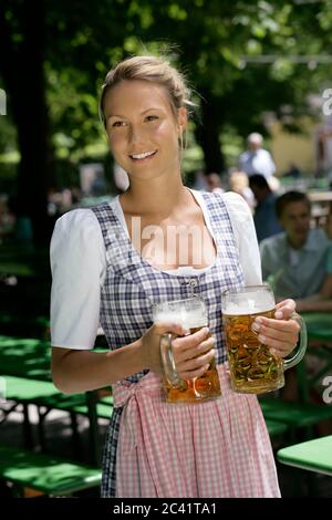 Jeune femme dans dirndl avec deux grandes tasses en main - service - café en plein air Banque D'Images