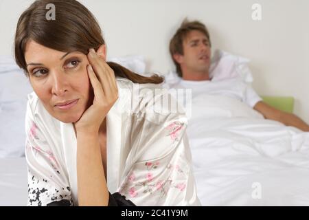 L'homme est dans le lit et dort, la femme est déçue sur le bord du lit Banque D'Images