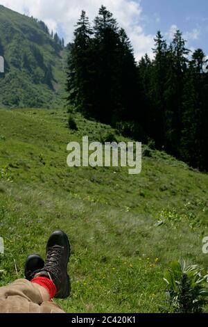 Les jambes d'un randonneur se trouvant dans un paysage de montagne et prenant une pause - Alpes Banque D'Images