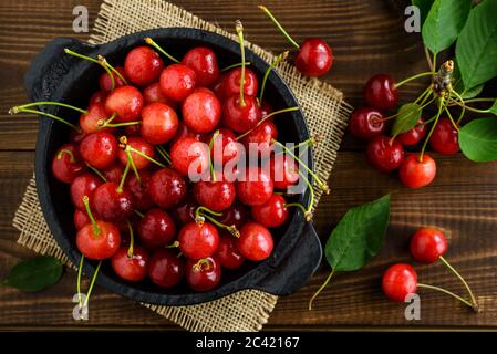 Cerises douces fraîches dans un bol noir et feuilles vertes sur une table en bois brun foncé. Vue de dessus. Banque D'Images