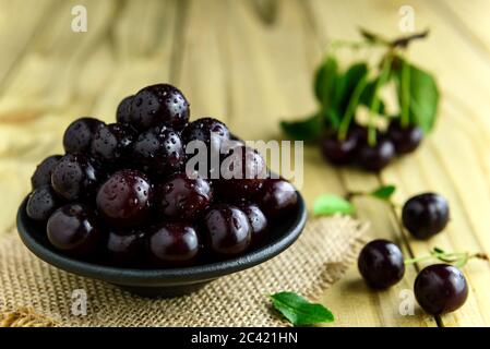 Cerises fraîches dans un bol noir et feuilles vertes sur la table en bois. Cerises fraîches mûres. Banque D'Images