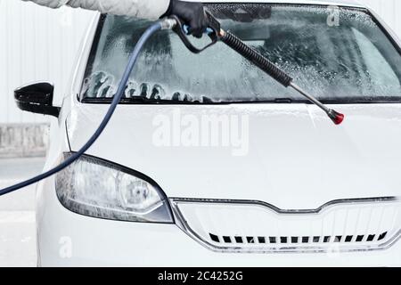 Gros plan d'une voiture dans une mousse au lavage manuel de voiture. Homme lavant une voiture sous haute pression dans une auto-lavage Banque D'Images