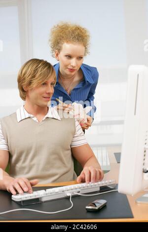Jeune homme travaillant sur l'ordinateur au bureau, jeune femme debout derrière lui avec de la nourriture chinoise Banque D'Images